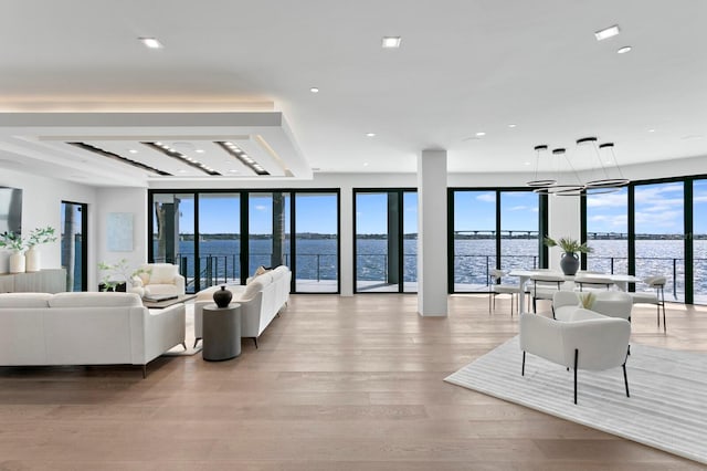 living room featuring floor to ceiling windows, light wood-type flooring, a water view, and a wealth of natural light