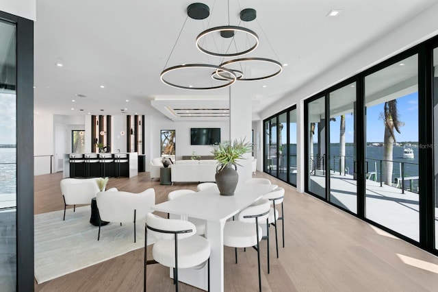 dining space with a water view, a chandelier, and light wood-type flooring