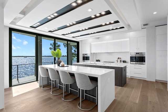 kitchen featuring a water view, white cabinetry, stainless steel oven, and an island with sink