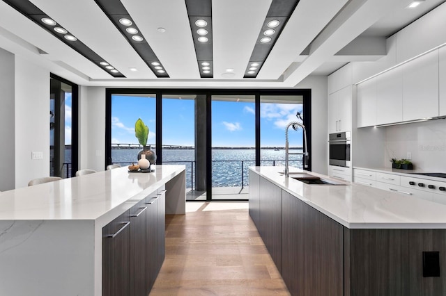 kitchen featuring stainless steel oven, white cabinets, a water view, a large island, and dark brown cabinetry