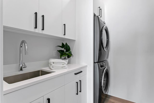 laundry area featuring dark hardwood / wood-style flooring, cabinets, stacked washer / dryer, and sink