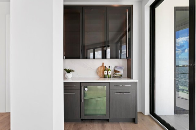 bar featuring backsplash, wine cooler, dark brown cabinetry, and light wood-type flooring