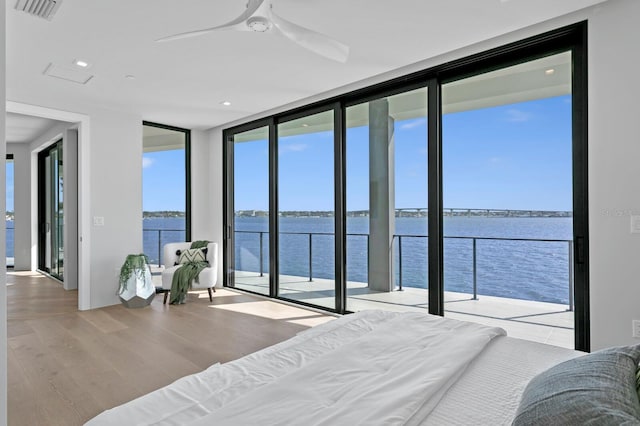 bedroom featuring wood-type flooring, a wall of windows, a water view, and ceiling fan