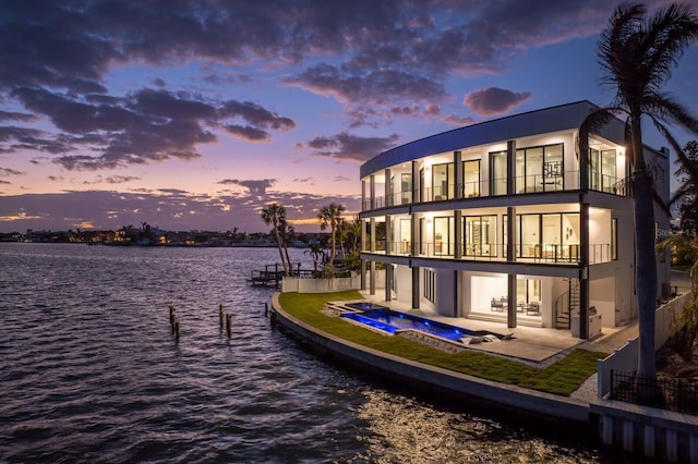 back house at dusk featuring a water view, a balcony, a patio, and a hot tub