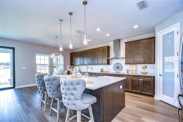 kitchen with wall chimney exhaust hood, sink, pendant lighting, a center island with sink, and a breakfast bar area