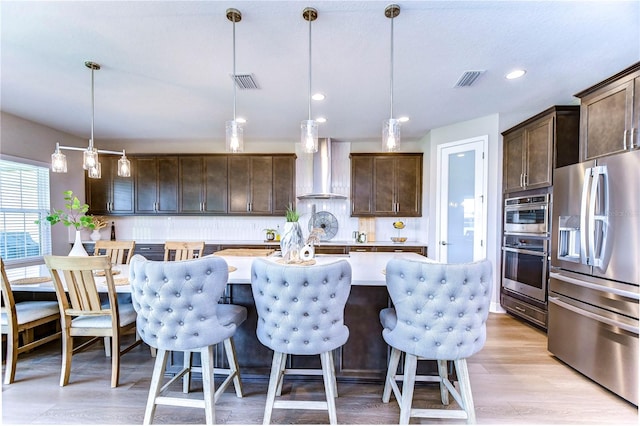 kitchen with pendant lighting, dark brown cabinets, wall chimney range hood, and appliances with stainless steel finishes