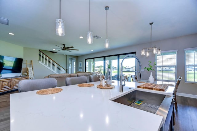 kitchen featuring a center island with sink, ceiling fan with notable chandelier, sink, decorative light fixtures, and dark hardwood / wood-style flooring