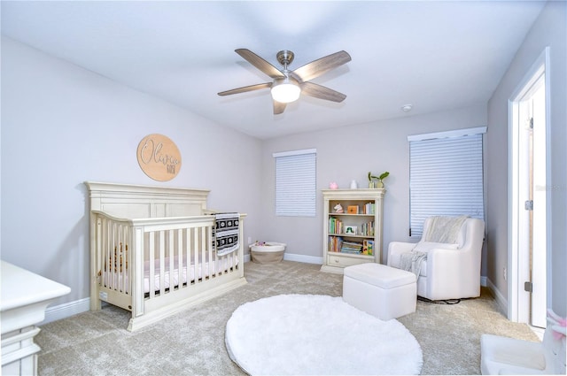 bedroom with a crib, light colored carpet, and ceiling fan