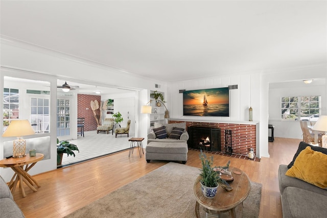 living room featuring a healthy amount of sunlight, light hardwood / wood-style floors, crown molding, and a brick fireplace