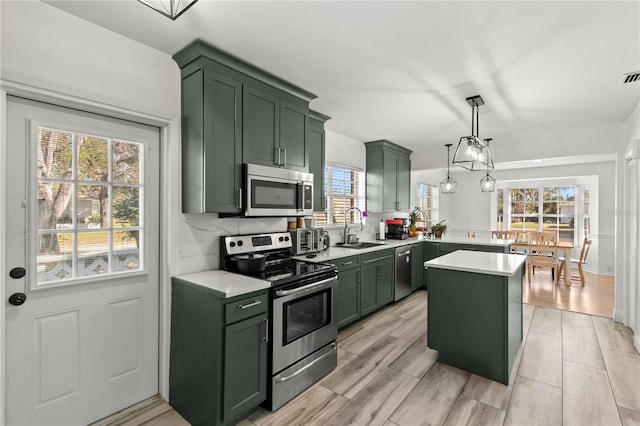 kitchen featuring appliances with stainless steel finishes, sink, a center island, hanging light fixtures, and green cabinets