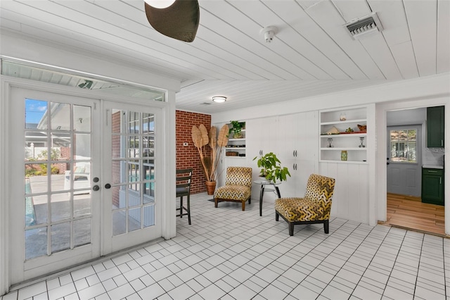 living area with built in features, light tile patterned floors, brick wall, and french doors