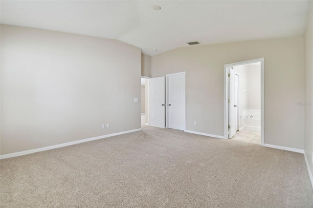 unfurnished bedroom featuring ensuite bathroom, light colored carpet, and lofted ceiling