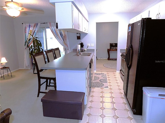 kitchen with white cabinets, ceiling fan, a textured ceiling, black fridge with ice dispenser, and a breakfast bar area