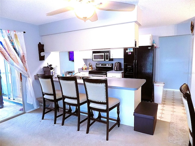 kitchen featuring a breakfast bar, white cabinets, ceiling fan, appliances with stainless steel finishes, and kitchen peninsula