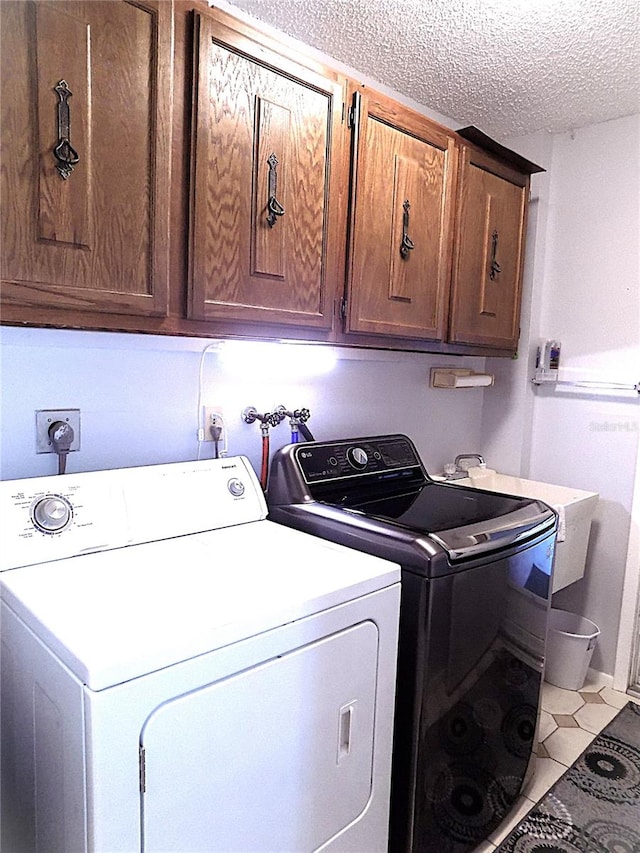 laundry room with cabinets, light tile patterned floors, washer and dryer, and a textured ceiling