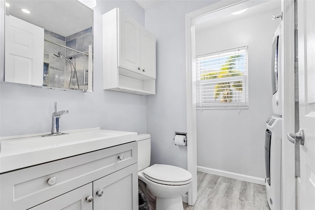 bathroom with hardwood / wood-style floors, vanity, stacked washer and clothes dryer, toilet, and tiled shower