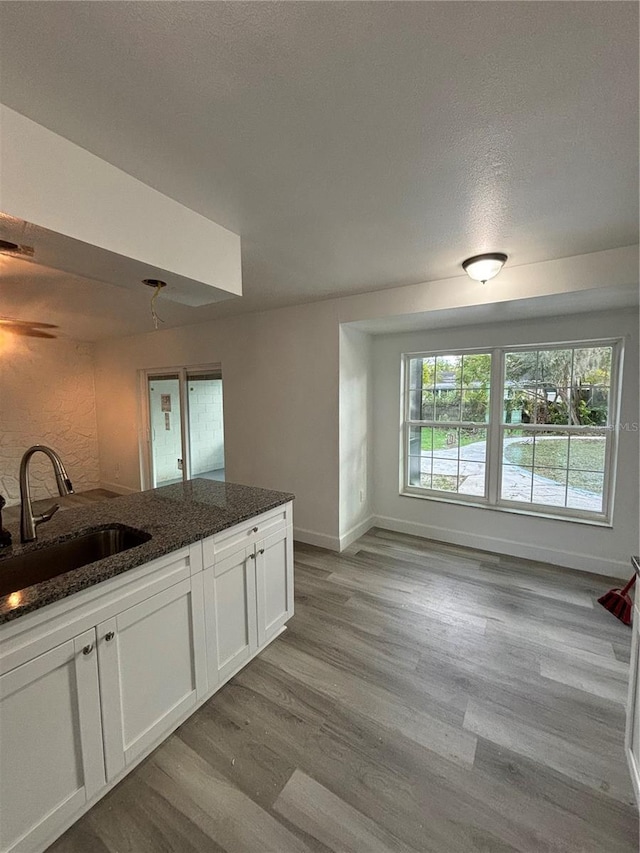 kitchen with light hardwood / wood-style floors, white cabinetry, dark stone countertops, and sink