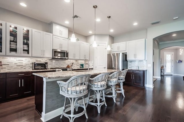 kitchen featuring decorative backsplash, dark hardwood / wood-style flooring, an island with sink, and appliances with stainless steel finishes