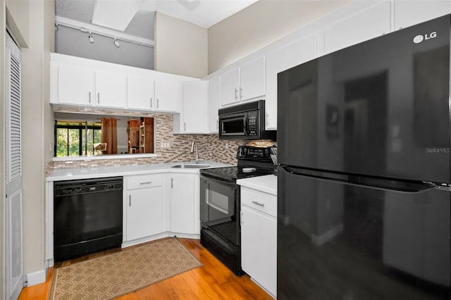 kitchen featuring tasteful backsplash, sink, black appliances, light hardwood / wood-style floors, and white cabinetry