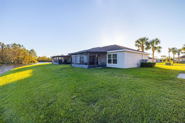 rear view of house with a sunroom, a water view, and a yard