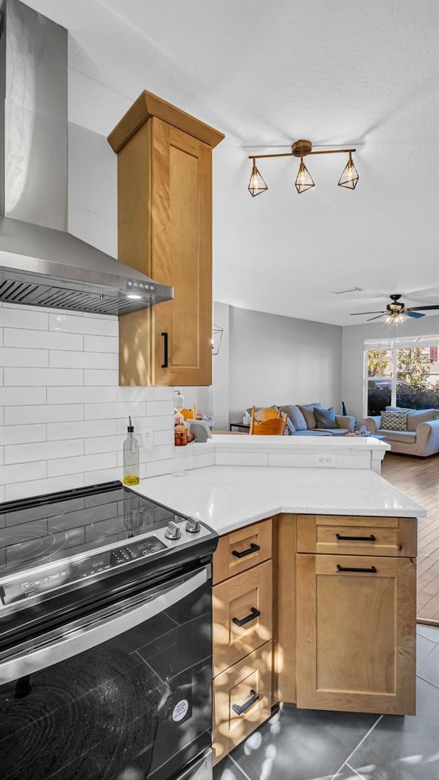 kitchen featuring kitchen peninsula, stainless steel range with electric stovetop, ceiling fan, dark tile patterned floors, and wall chimney range hood