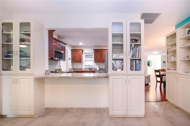 kitchen featuring light wood-type flooring, light stone countertops, and kitchen peninsula