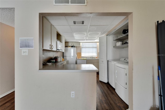 kitchen with white appliances, sink, dark hardwood / wood-style floors, washing machine and dryer, and kitchen peninsula