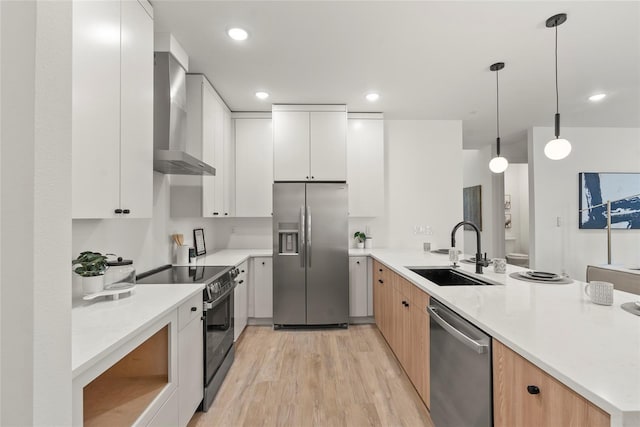 kitchen featuring sink, wall chimney exhaust hood, decorative light fixtures, white cabinetry, and stainless steel appliances