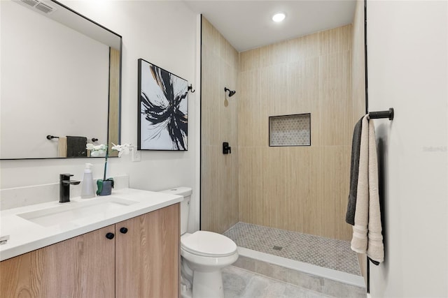 bathroom with tile patterned flooring, a tile shower, vanity, and toilet