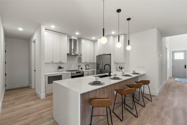 kitchen with white cabinets, decorative light fixtures, wall chimney range hood, and stainless steel appliances