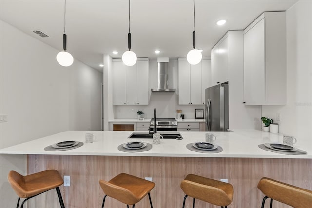 kitchen featuring wall chimney exhaust hood, sink, white cabinets, stainless steel refrigerator, and hanging light fixtures