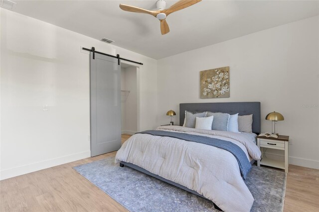 bedroom with hardwood / wood-style flooring, ceiling fan, and a barn door