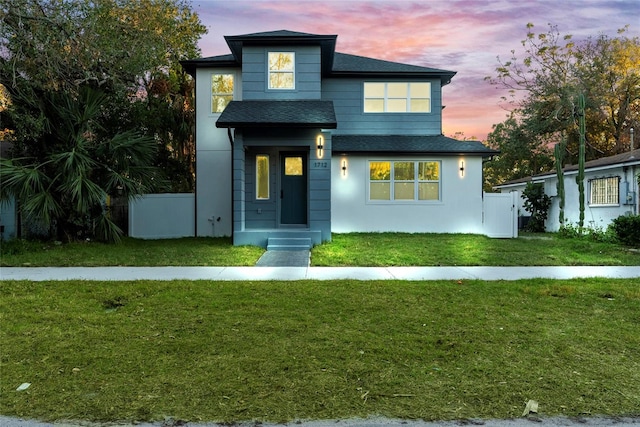 view of front facade with a shingled roof, a front yard, and fence