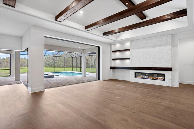 unfurnished living room featuring baseboards, a sunroom, beamed ceiling, wood finished floors, and a stone fireplace