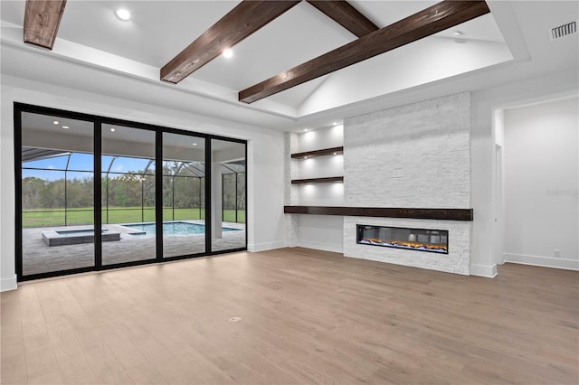 unfurnished living room with vaulted ceiling with beams, built in shelves, a stone fireplace, wood finished floors, and visible vents