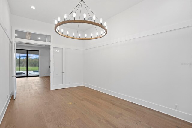 spare room with recessed lighting, baseboards, a notable chandelier, and wood finished floors