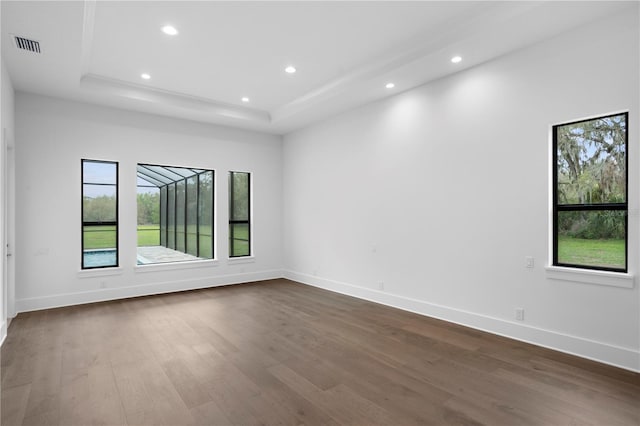 spare room featuring dark wood-style flooring, recessed lighting, a raised ceiling, visible vents, and baseboards