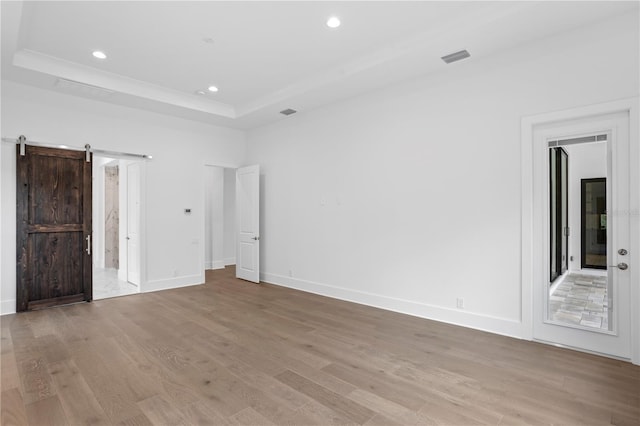 spare room with light wood finished floors, recessed lighting, a raised ceiling, a barn door, and baseboards