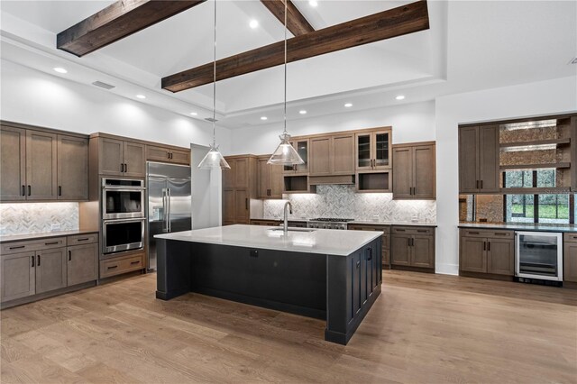 kitchen with wine cooler, light wood finished floors, stainless steel appliances, a sink, and high vaulted ceiling