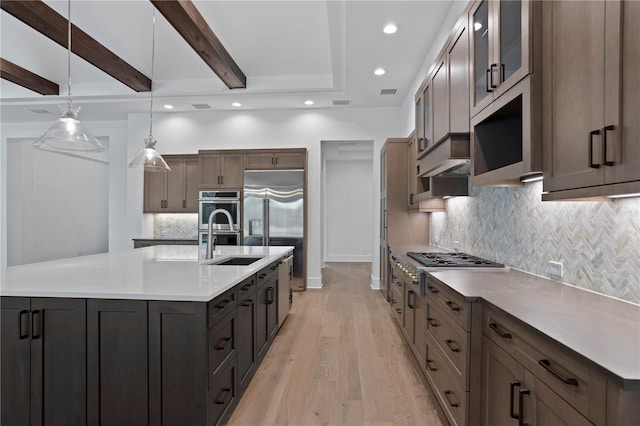 kitchen featuring stainless steel appliances, a sink, a large island, light wood-type flooring, and beam ceiling