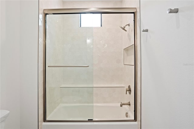 bathroom featuring combined bath / shower with glass door and toilet