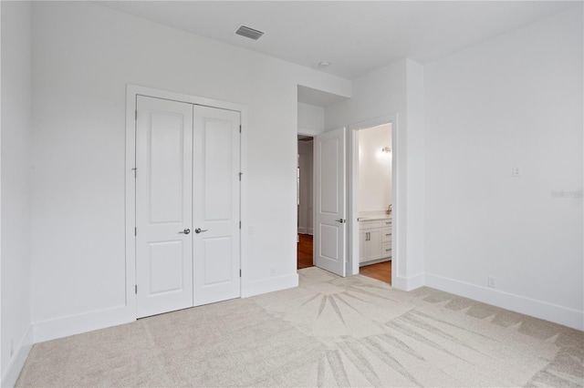 unfurnished bedroom featuring connected bathroom, light colored carpet, visible vents, baseboards, and a closet