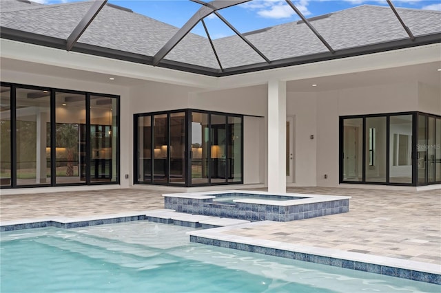 rear view of house featuring a lanai, a shingled roof, a pool with connected hot tub, stucco siding, and a patio area