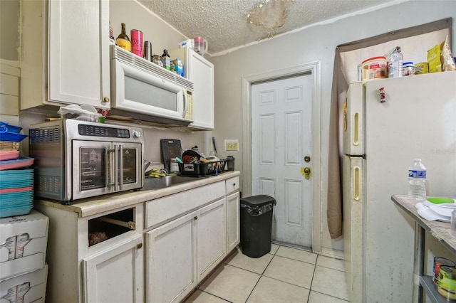 kitchen featuring a textured ceiling, white cabinetry, light tile patterned flooring, and white appliances