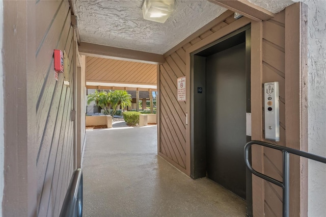 hall featuring wood walls, a textured ceiling, and elevator