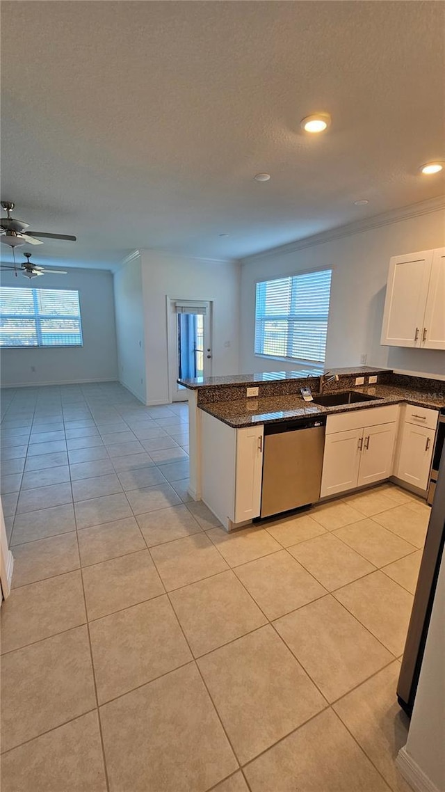 kitchen with sink, light tile patterned floors, stainless steel dishwasher, dark stone countertops, and white cabinets