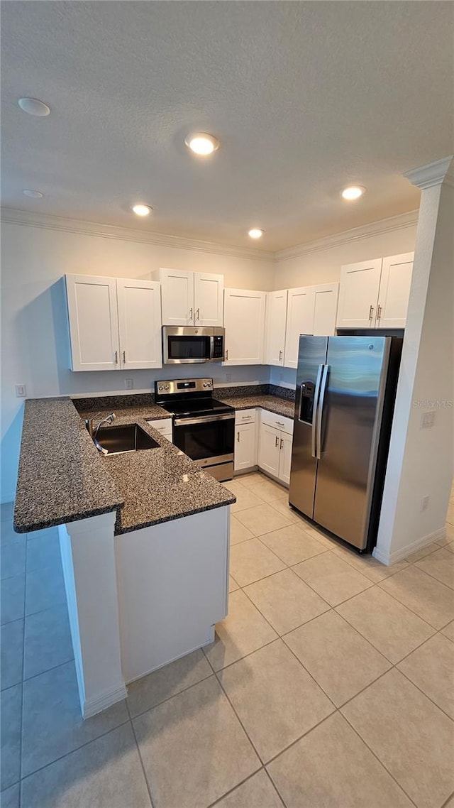 kitchen with kitchen peninsula, appliances with stainless steel finishes, sink, dark stone countertops, and white cabinetry