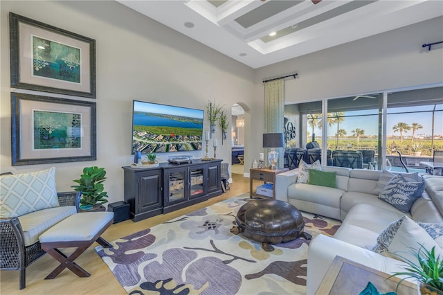 living room with beamed ceiling, light wood-type flooring, a towering ceiling, and coffered ceiling