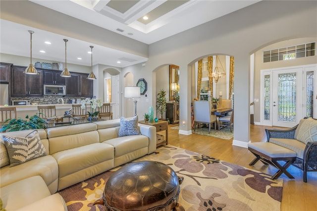 living room with beam ceiling, an inviting chandelier, coffered ceiling, and light wood-type flooring