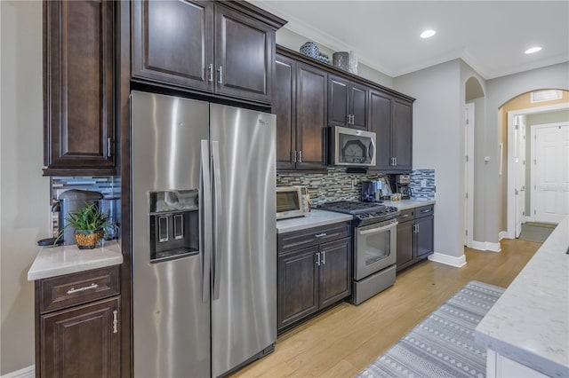 kitchen with backsplash, ornamental molding, dark brown cabinetry, stainless steel appliances, and light hardwood / wood-style floors